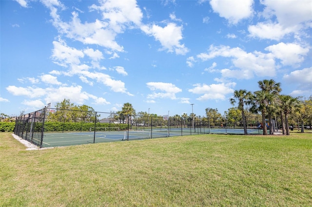 view of tennis court with a lawn and fence