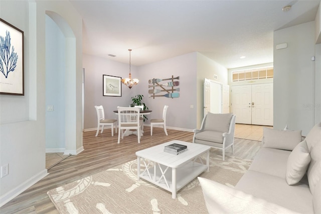 living room with light wood-type flooring, visible vents, arched walkways, baseboards, and a chandelier