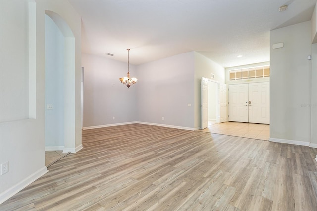 spare room with an inviting chandelier, light wood-style floors, and baseboards