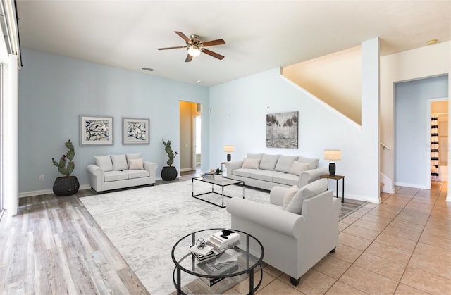 living room with visible vents, baseboards, ceiling fan, stairway, and light wood-style flooring