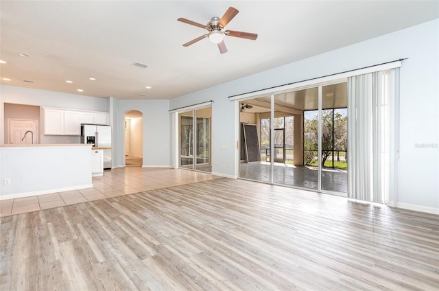 unfurnished living room with visible vents, recessed lighting, arched walkways, ceiling fan, and light wood-style floors