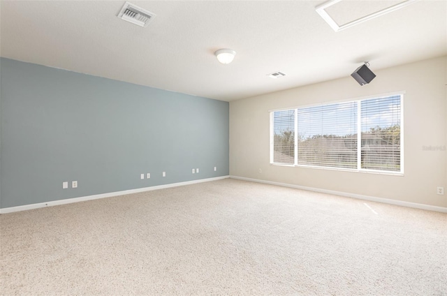 unfurnished room with visible vents, baseboards, attic access, and light carpet