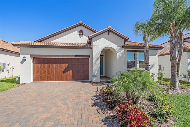 mediterranean / spanish house featuring a tile roof, decorative driveway, an attached garage, and stucco siding