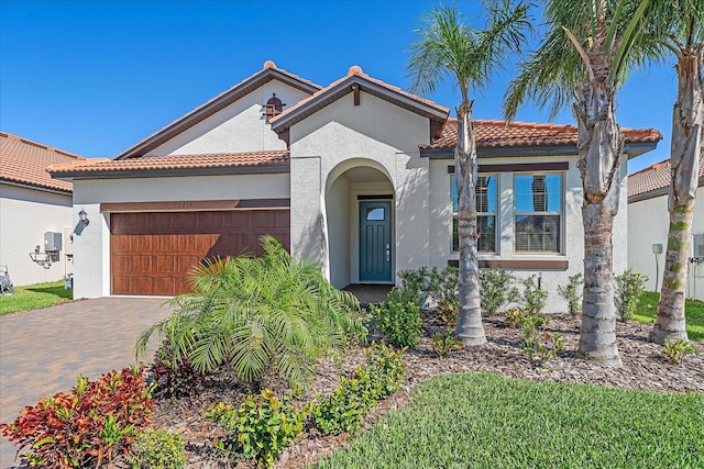 mediterranean / spanish house with a tiled roof, stucco siding, an attached garage, and decorative driveway