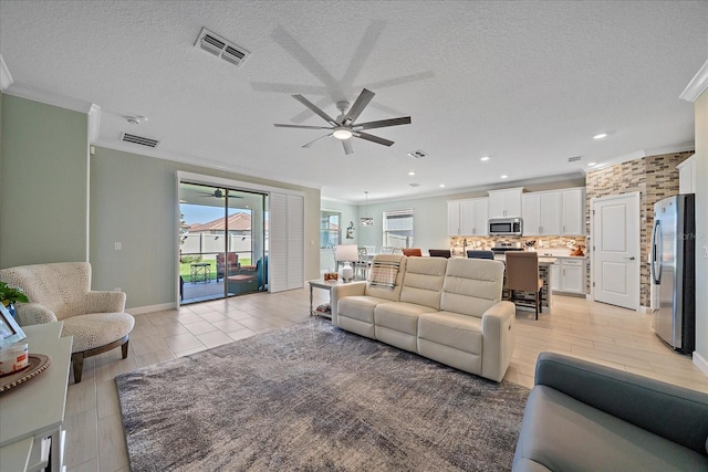 living area with visible vents, a textured ceiling, a healthy amount of sunlight, and ornamental molding