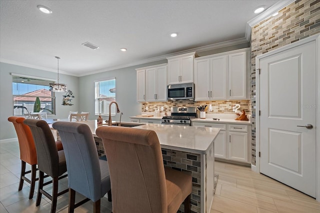 kitchen with visible vents, a kitchen island with sink, a sink, appliances with stainless steel finishes, and crown molding