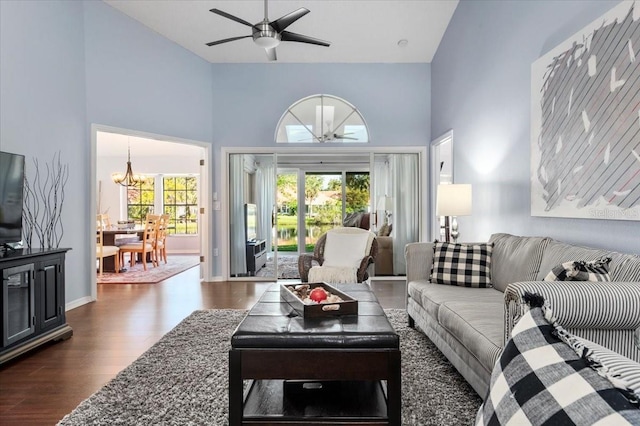 living room with dark wood finished floors, ceiling fan with notable chandelier, baseboards, and a towering ceiling