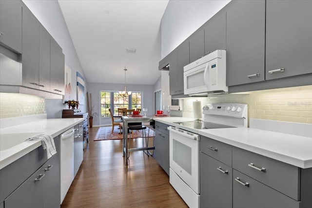 kitchen with a chandelier, vaulted ceiling, gray cabinets, dark wood-style floors, and white appliances