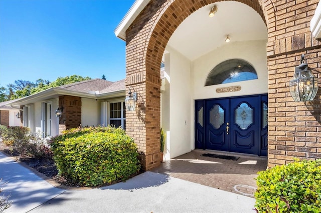 property entrance with stucco siding, brick siding, and roof with shingles