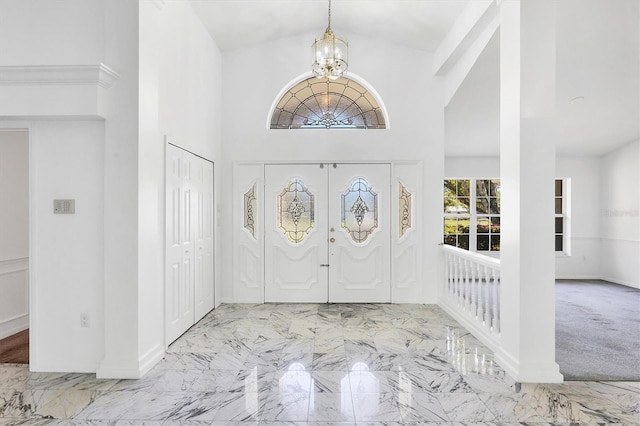 foyer entrance featuring baseboards, marble finish floor, a towering ceiling, and a chandelier