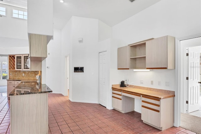 kitchen featuring backsplash, light tile patterned floors, a peninsula, a high ceiling, and built in study area