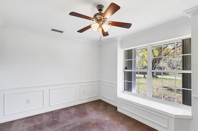 spare room with a wealth of natural light, dark colored carpet, ornamental molding, and a ceiling fan