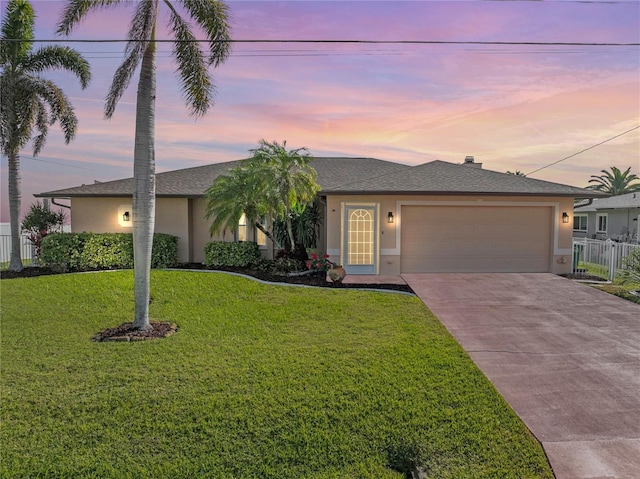 ranch-style house featuring a yard, stucco siding, driveway, an attached garage, and fence