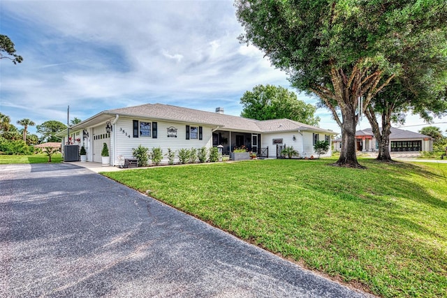 ranch-style home featuring aphalt driveway, central AC unit, an attached garage, and a front yard