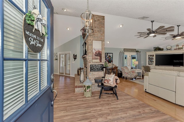 entrance foyer featuring light wood finished floors, visible vents, ceiling fan with notable chandelier, a fireplace, and a textured ceiling