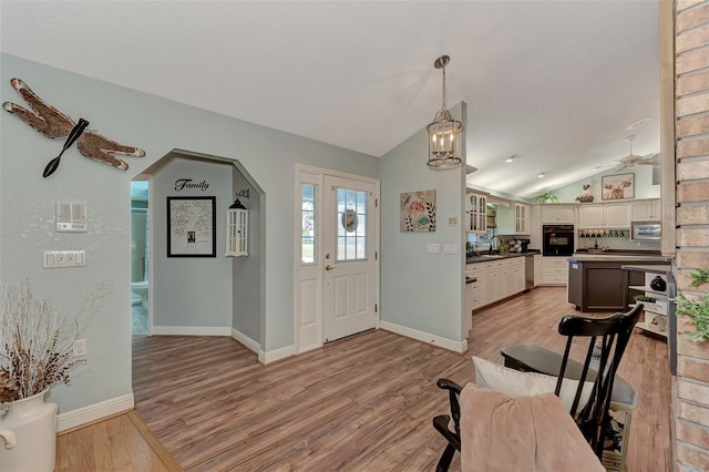 foyer featuring baseboards, light wood-style floors, arched walkways, and vaulted ceiling