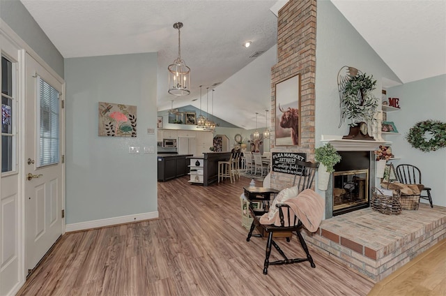 living room featuring baseboards, lofted ceiling, a fireplace, an inviting chandelier, and wood finished floors