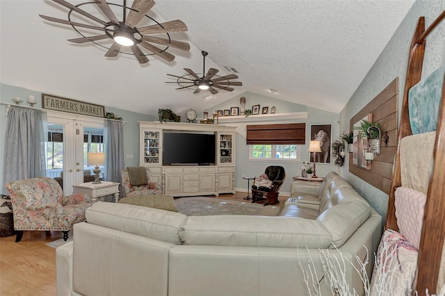 living area featuring light wood-type flooring, lofted ceiling, french doors, a textured ceiling, and a ceiling fan