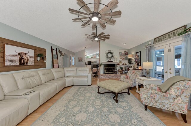 living area with light wood-type flooring, french doors, a brick fireplace, ceiling fan, and vaulted ceiling