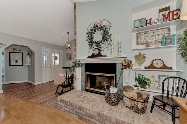 interior space featuring wood finished floors, arched walkways, a fireplace, baseboards, and vaulted ceiling