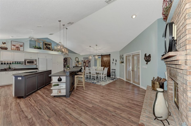 kitchen with stainless steel microwave, a kitchen island, dark countertops, lofted ceiling, and a brick fireplace