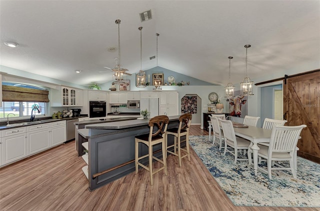 kitchen with visible vents, a kitchen island, stainless steel appliances, vaulted ceiling, and dark countertops