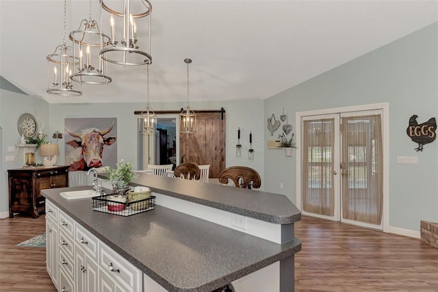 kitchen with wood finished floors, a barn door, a sink, dark countertops, and a center island