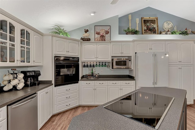 kitchen with black appliances, light wood-style flooring, dark countertops, glass insert cabinets, and lofted ceiling