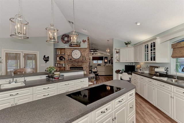 kitchen featuring a sink, dark countertops, black electric cooktop, lofted ceiling, and a brick fireplace