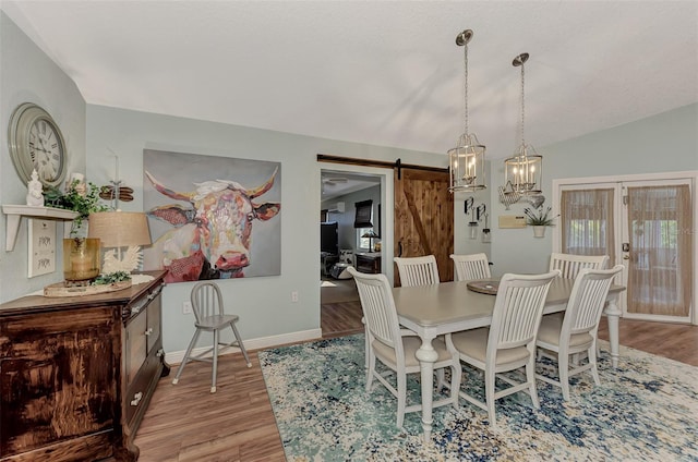 dining space with baseboards, lofted ceiling, a barn door, and wood finished floors