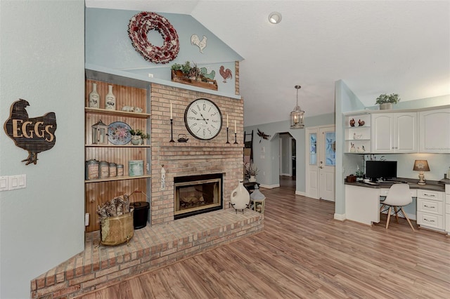 living area with a fireplace, built in study area, light wood-type flooring, and vaulted ceiling