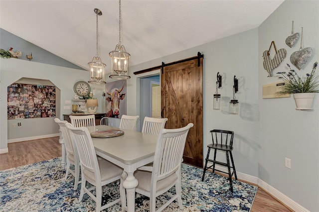 dining area featuring baseboards, a barn door, vaulted ceiling, wood finished floors, and arched walkways