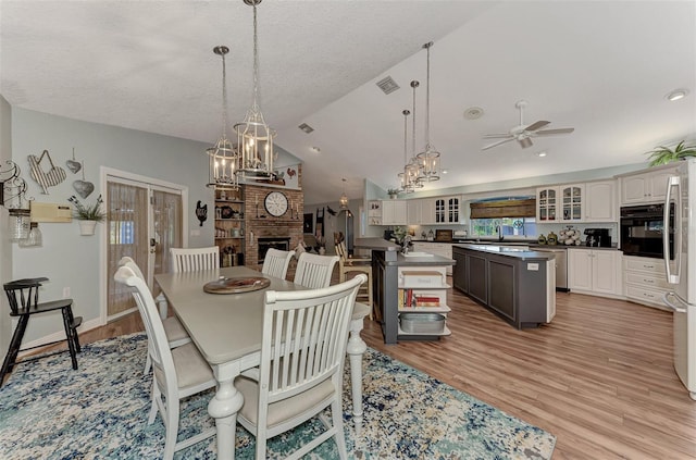 dining room with light wood-style flooring, a fireplace, ceiling fan with notable chandelier, and lofted ceiling