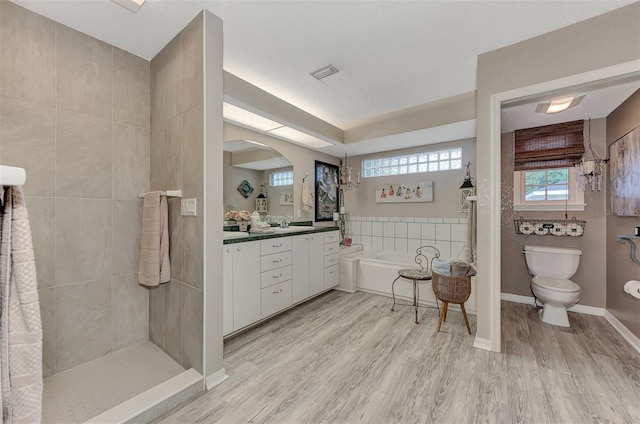 bathroom with visible vents, toilet, wood finished floors, a bath, and vanity