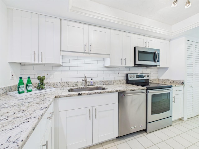 kitchen with a sink, light stone counters, tasteful backsplash, white cabinetry, and appliances with stainless steel finishes