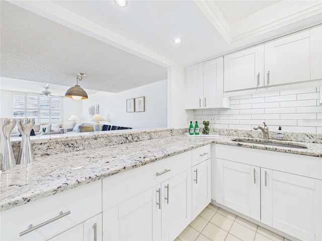 kitchen with light stone counters, a sink, white cabinetry, tasteful backsplash, and open floor plan