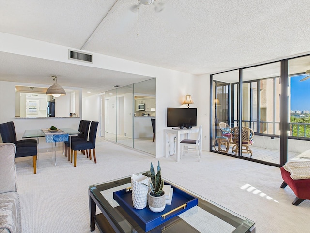 carpeted living area with ceiling fan, visible vents, and a textured ceiling