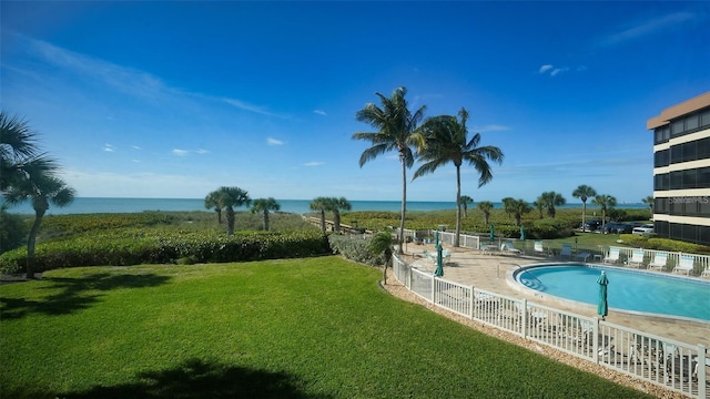 community pool featuring a yard, a water view, and fence