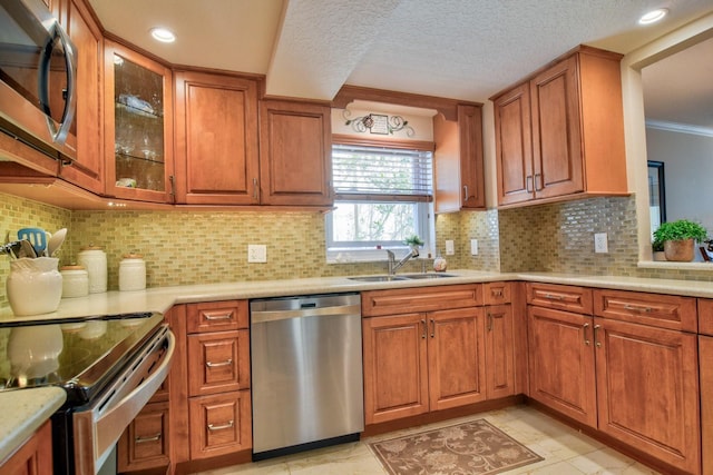 kitchen with light countertops, ornamental molding, brown cabinets, appliances with stainless steel finishes, and a sink