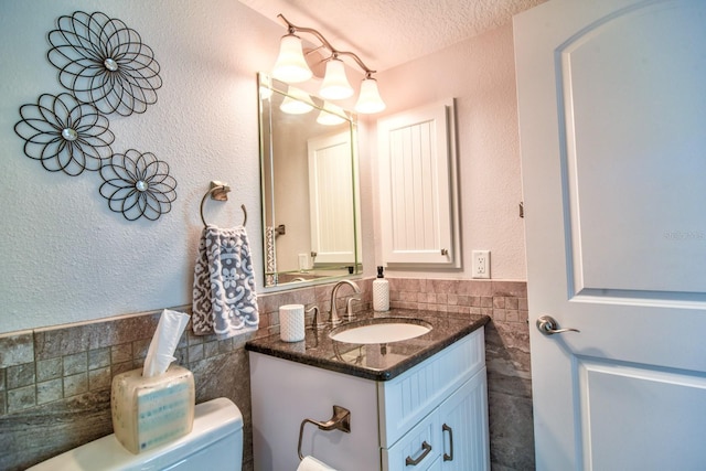 bathroom with a wainscoted wall, toilet, a textured ceiling, tile walls, and vanity