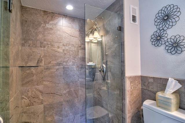 full bath featuring visible vents, toilet, a walk in shower, a textured ceiling, and tile walls