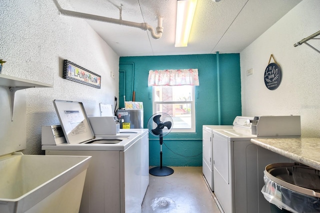 laundry room featuring washer and dryer, a textured ceiling, a sink, and a textured wall