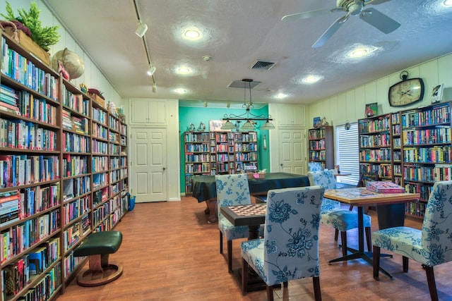 living area featuring visible vents, a textured ceiling, wood finished floors, and wall of books