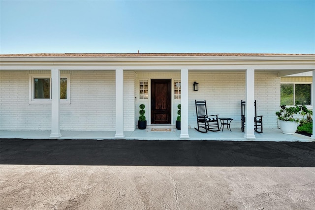 view of exterior entry featuring brick siding and covered porch