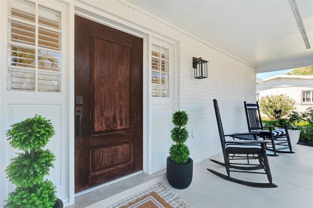 doorway to property featuring a porch and brick siding