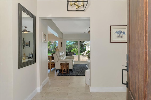 corridor with an inviting chandelier, light tile patterned floors, and baseboards