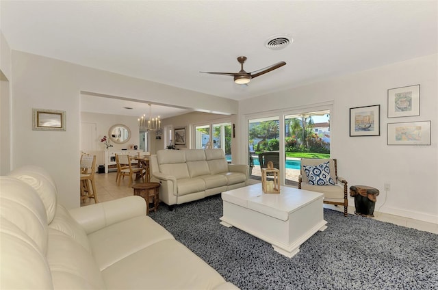 living area featuring tile patterned floors, visible vents, baseboards, and ceiling fan with notable chandelier