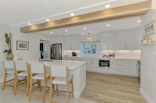 kitchen featuring beam ceiling, a kitchen breakfast bar, stainless steel appliances, white cabinetry, and a sink