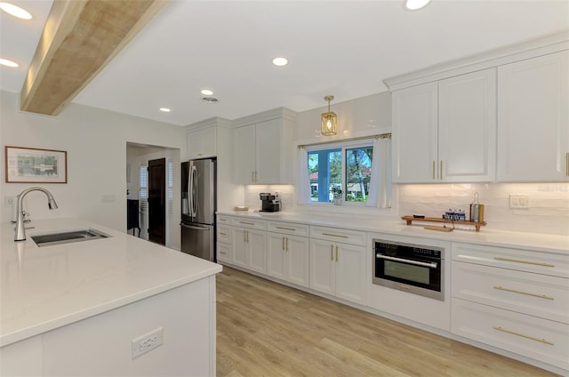 kitchen featuring a sink, oven, white cabinets, stainless steel refrigerator with ice dispenser, and tasteful backsplash