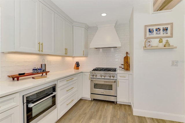 kitchen featuring light wood-type flooring, appliances with stainless steel finishes, white cabinets, light countertops, and custom exhaust hood